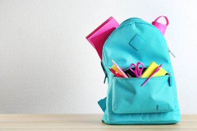 Photo of Bright backpack with different school stationery on wooden table against white background. Space for text
