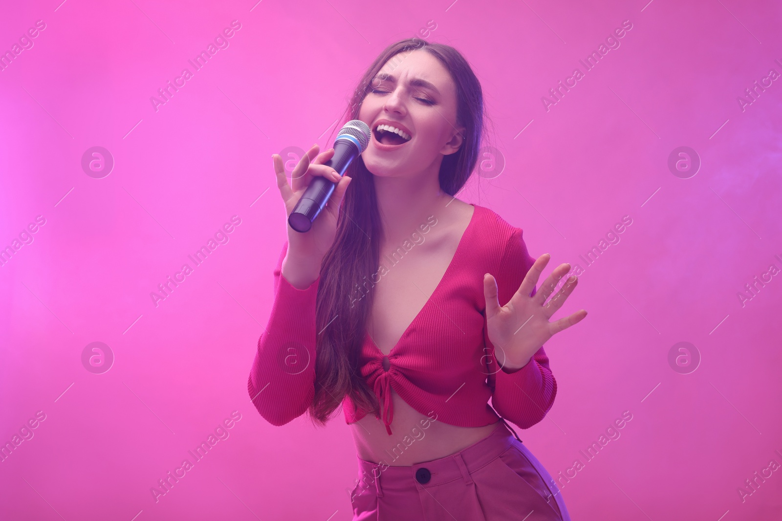 Photo of Emotional woman with microphone singing on pink background