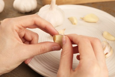 Woman peeling fresh garlic at table, closeup