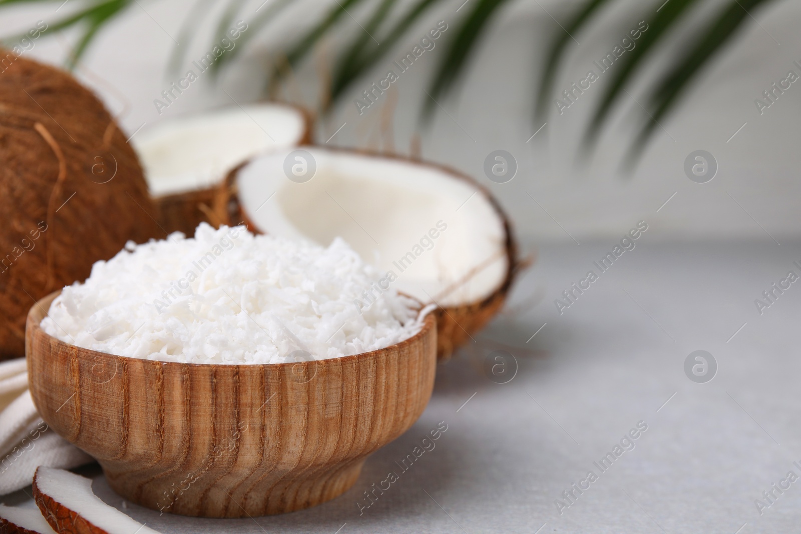 Photo of Coconut flakes in bowl and nuts on light grey table, space for text