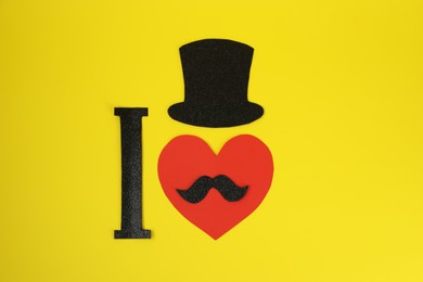 Photo of I Love Mustache. FLat lay composition of paper hat and heart on yellow background