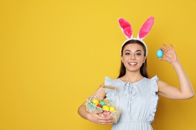 Photo of Beautiful woman in bunny ears headband with Easter eggs on color background, space for text