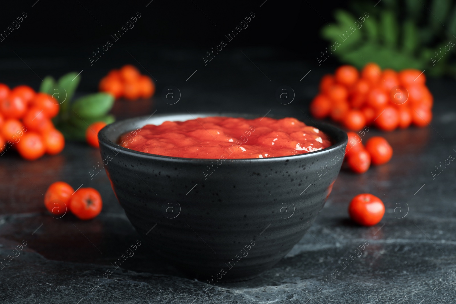 Photo of Delicious rowan jam in ceramic bowl on dark table, closeup