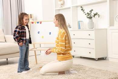 Photo of Mom teaching her daughter alphabet with magnetic letters at home