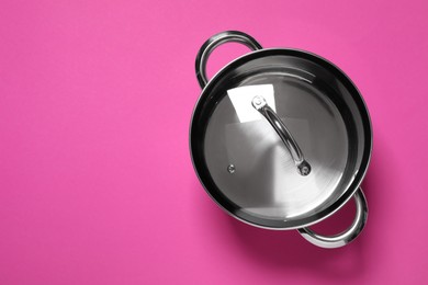 Steel pot with glass lid on dark pink background, top view. Space for text