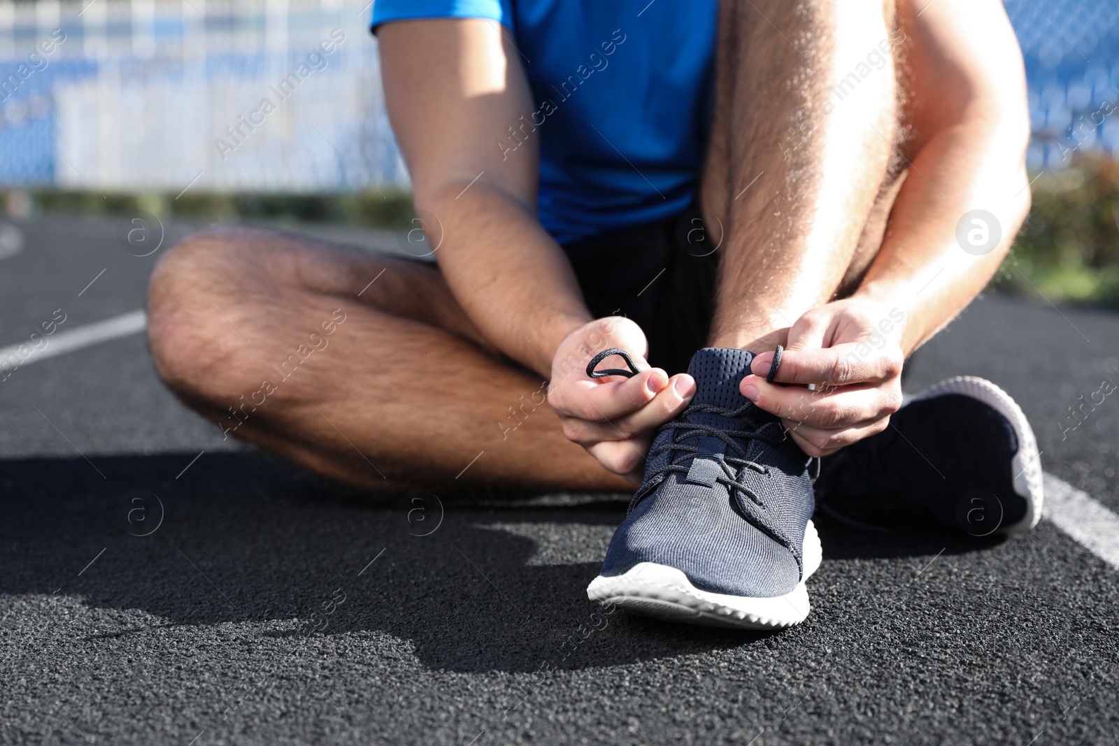 Image of Sporty man tying shoelaces at stadium on sunny morning, closeup