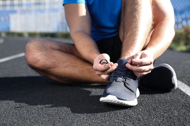 Sporty man tying shoelaces at stadium on sunny morning, closeup