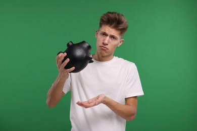 Photo of Upset man with empty piggy bank on green background