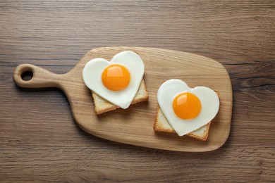 Photo of Heart shaped fried eggs and toasts on wooden table, top view