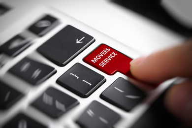 Woman pressing button with phrase MOVERS SERVICE on laptop keyboard, closeup