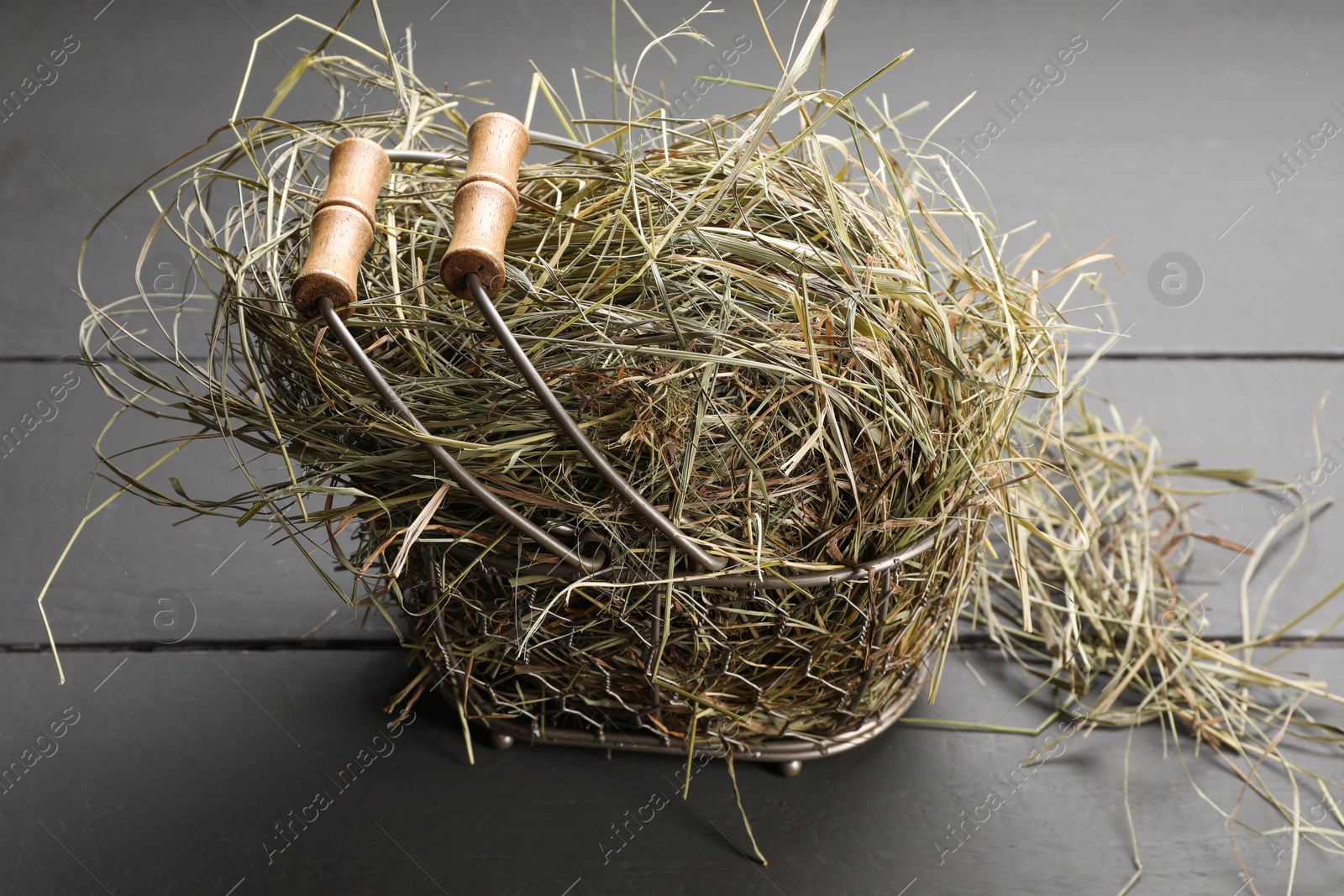 Photo of Dried hay in metal basket on grey wooden table