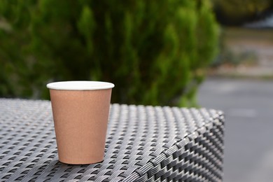 Photo of Coffee cardboard cup on rattan table outdoors, space for text