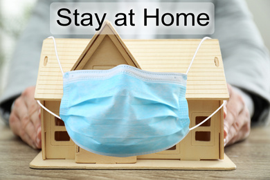 Image of Stay at home during coronavirus quarantine. Man and wooden house model with medical mask
