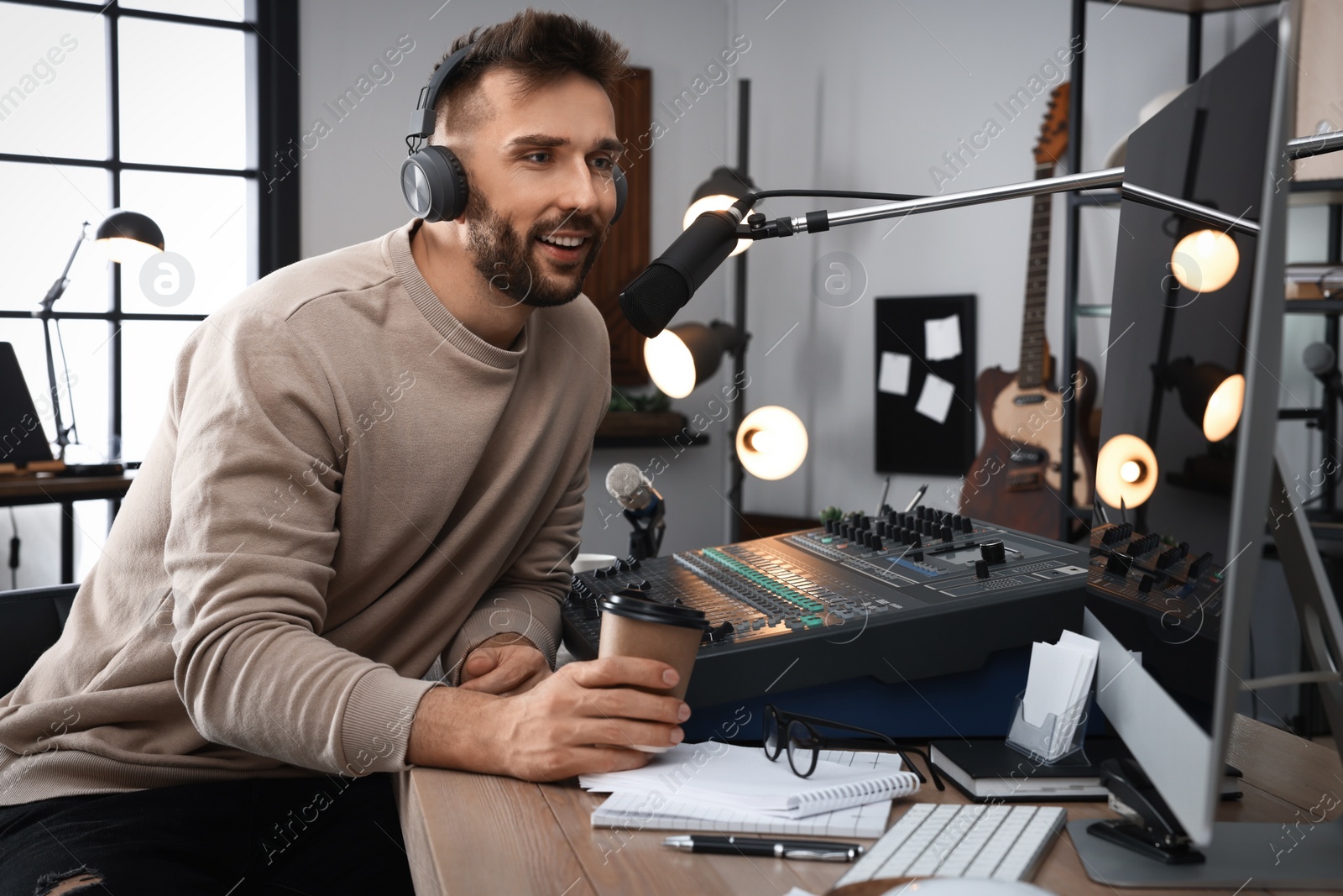 Photo of Man with cup of coffee working as radio host in modern studio