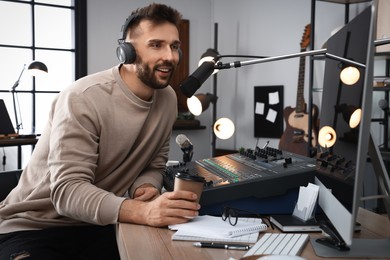 Photo of Man with cup of coffee working as radio host in modern studio