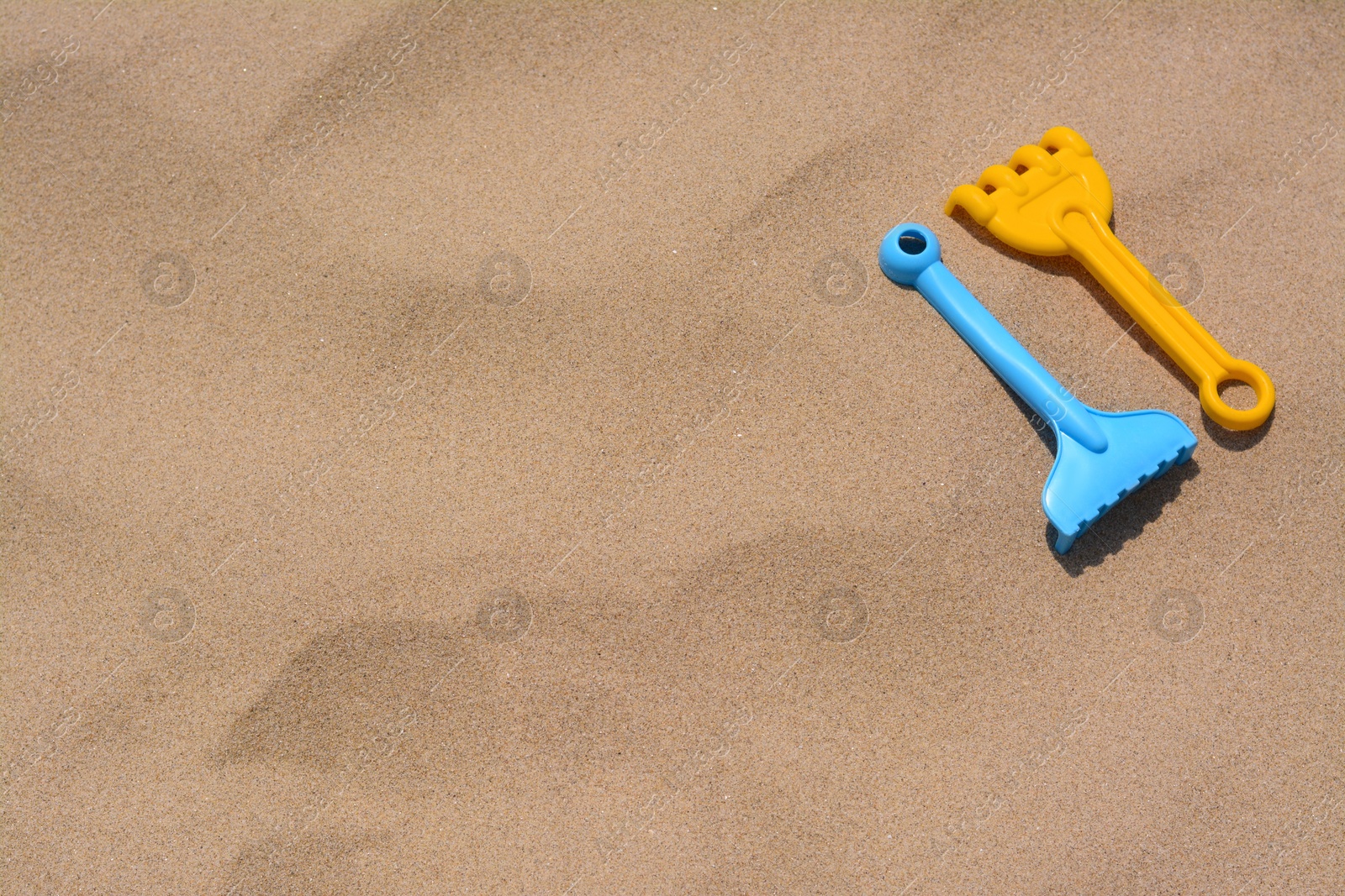 Photo of Colorful plastic rakes on sand, space for text. Beach toys