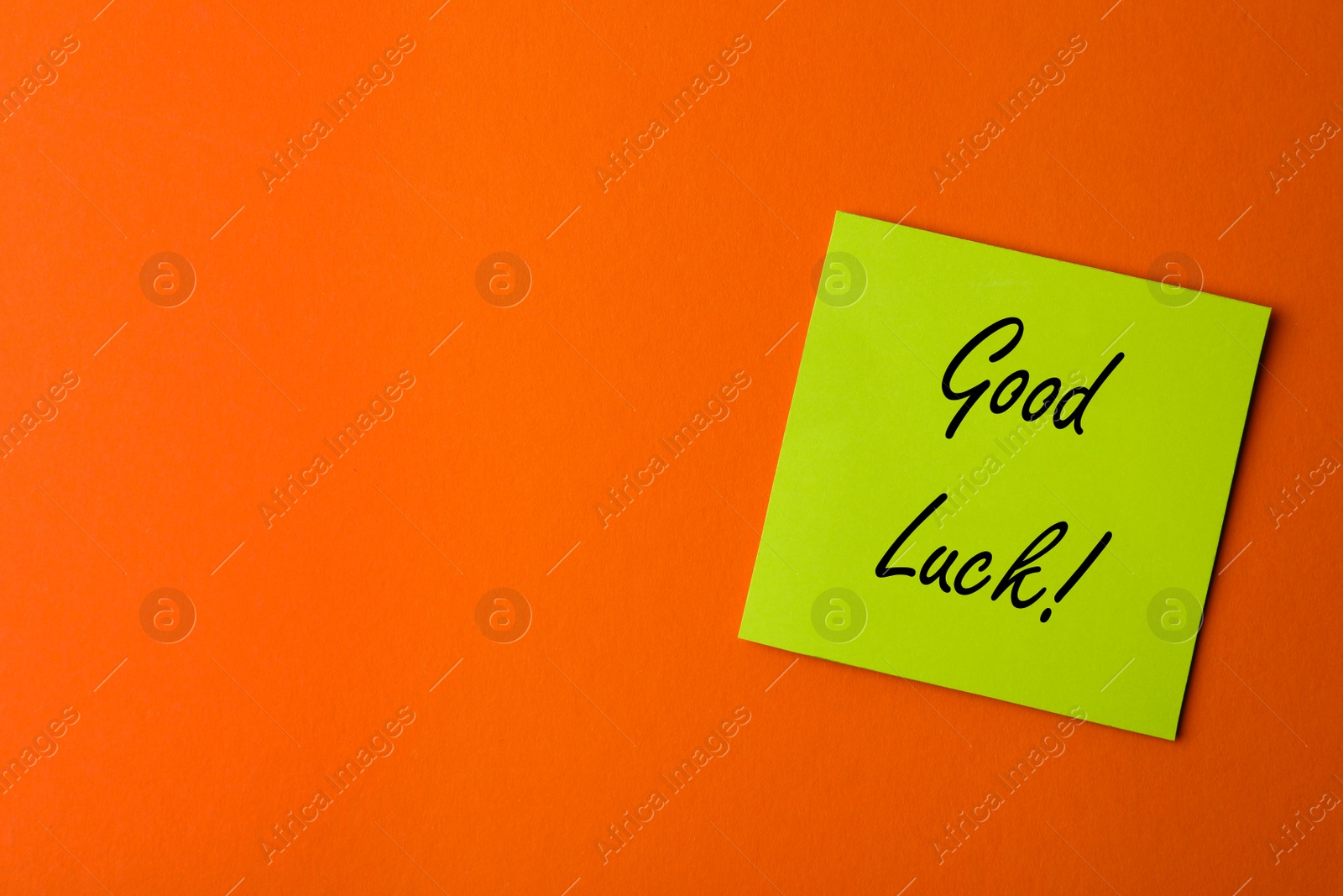 Image of Green note with phrase GOOD LUCK on orange background, top view. Space for text