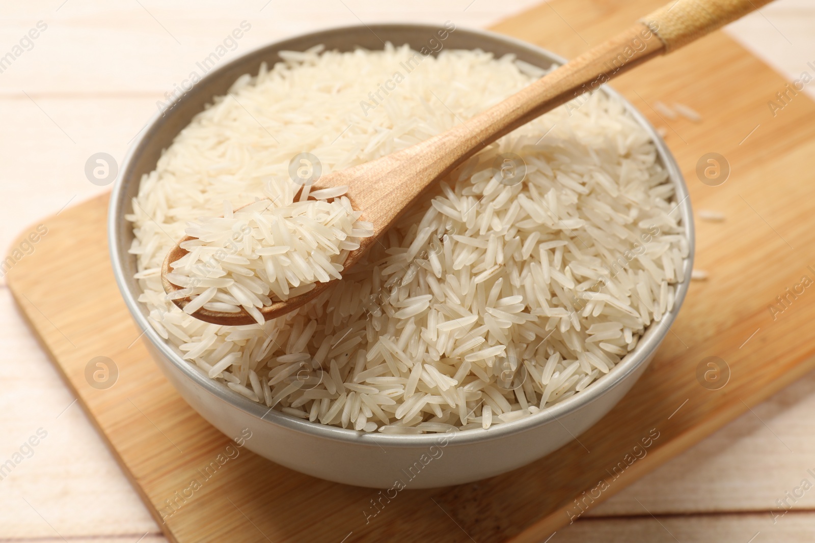 Photo of Raw basmati rice and spoon in bowl on wooden table