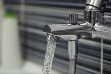 Photo of Water flowing from bath tap on blurred background, closeup