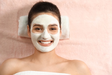 Photo of Beautiful woman with white mask on face relaxing in spa salon, top view