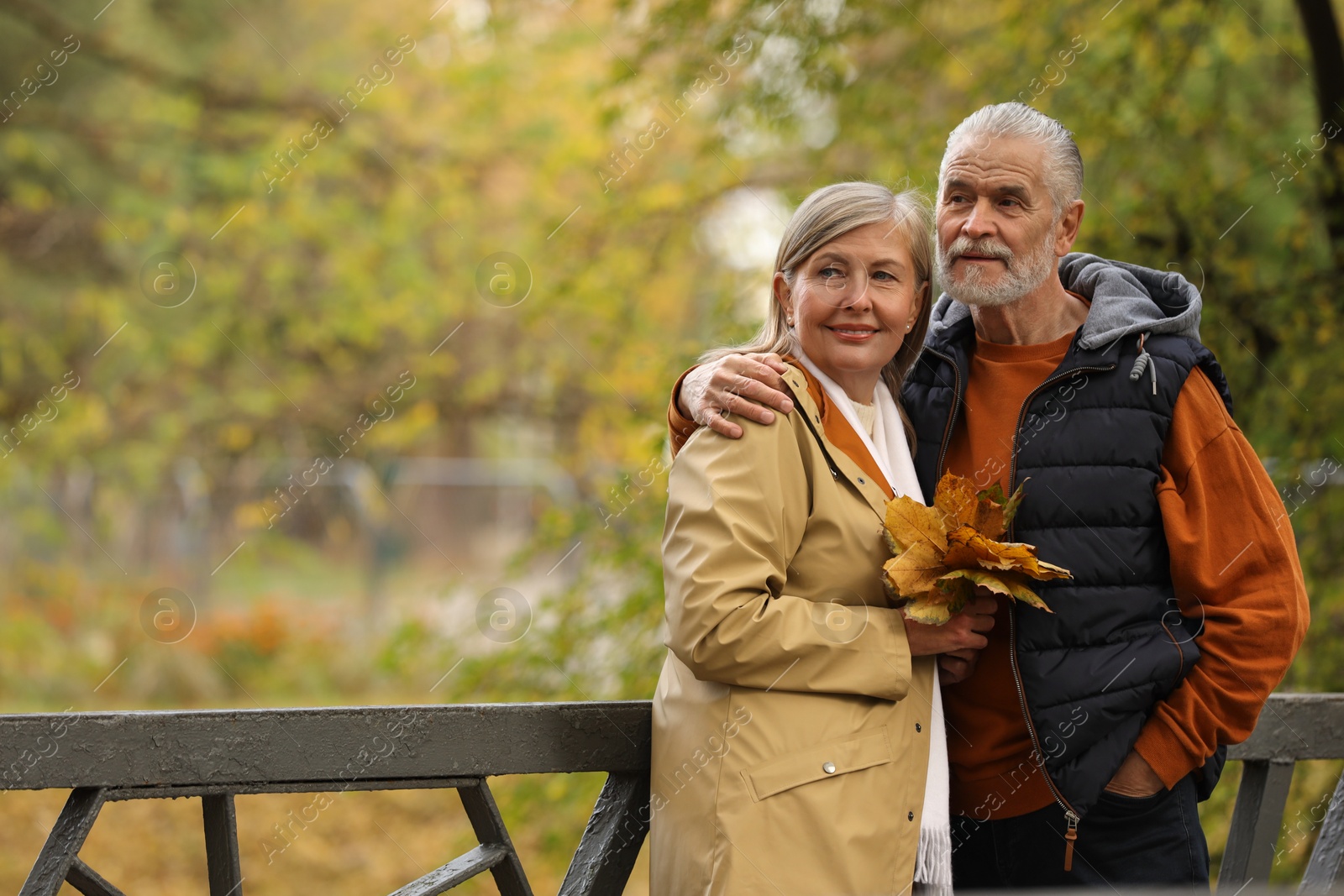 Photo of Affectionate senior couple with dry leaves in autumn park, space for text