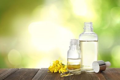 Image of Bottles of essential oil and flowers on wooden table against blurred background. Space for text