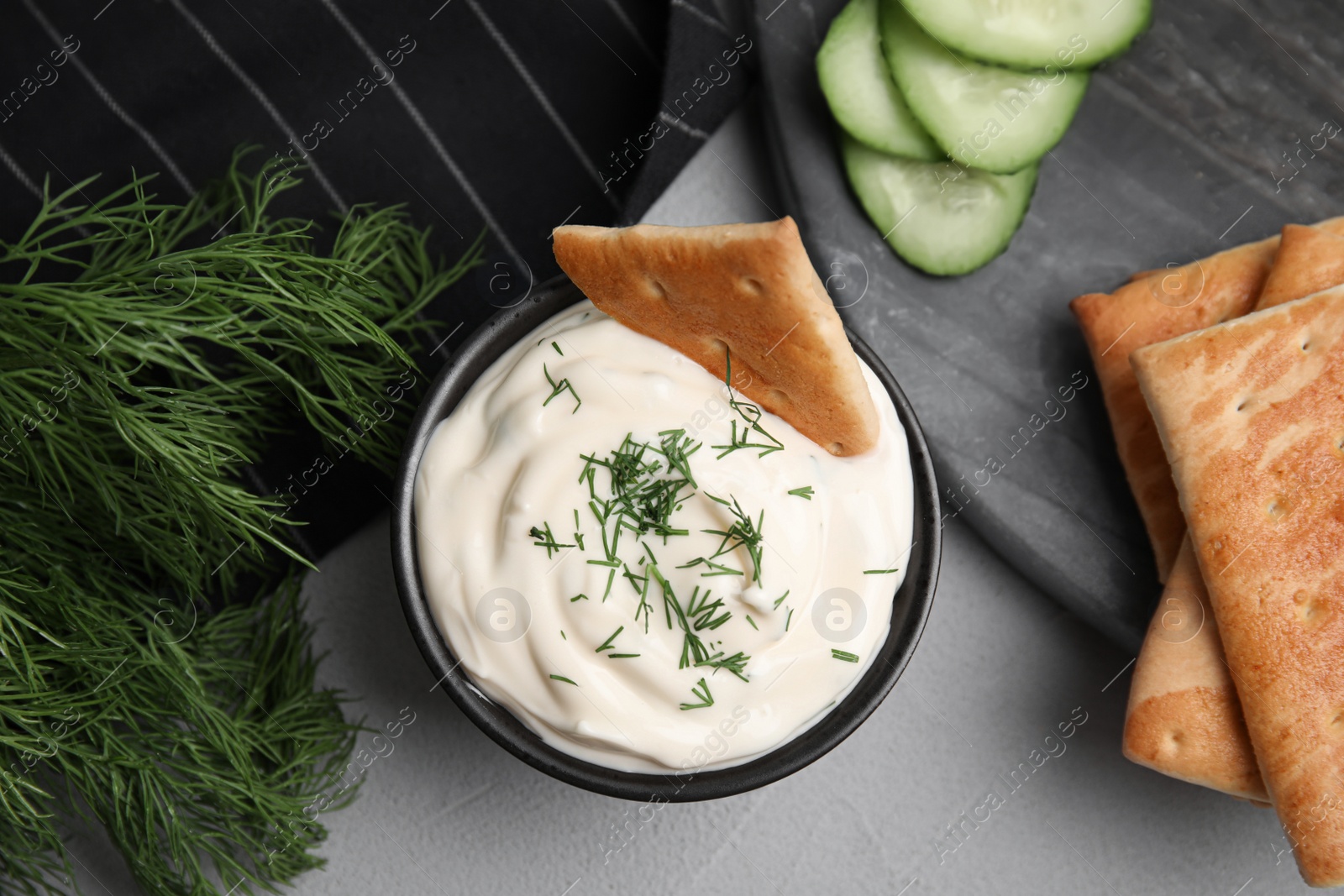 Photo of Tasty creamy dill sauce, crackers and ingredients on grey table, flat lay