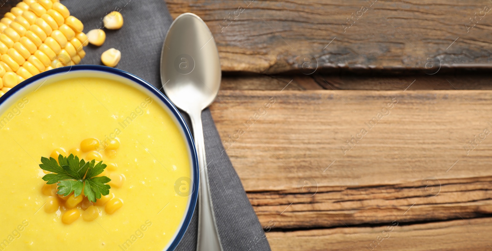 Photo of Delicious creamy corn soup served on wooden table, top view. Space for text