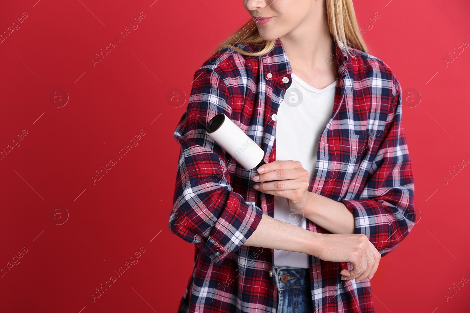 Photo of Young woman cleaning clothes with lint roller on red background, closeup