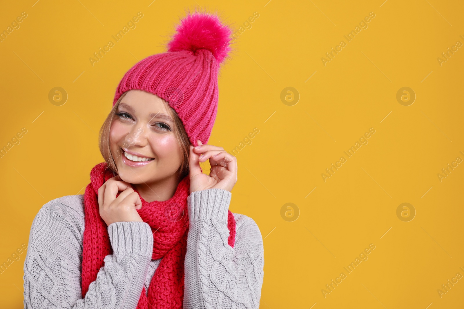 Photo of Young woman in warm sweater, scarf and hat on yellow background, space for text. Winter season