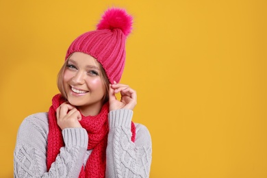 Photo of Young woman in warm sweater, scarf and hat on yellow background, space for text. Winter season