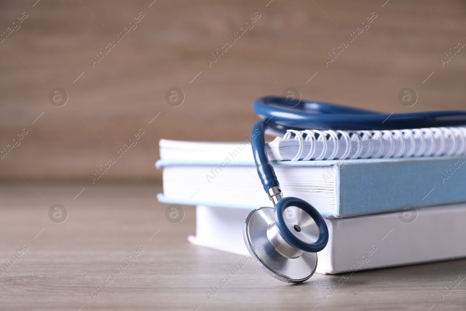 Photo of Closeup view of student textbooks and stethoscope on wooden table, space for text. Medical education