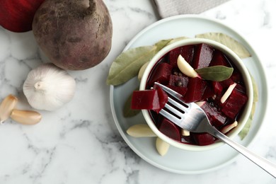 Photo of Pickled beets with garlic in bowl on white marble table, flat lay