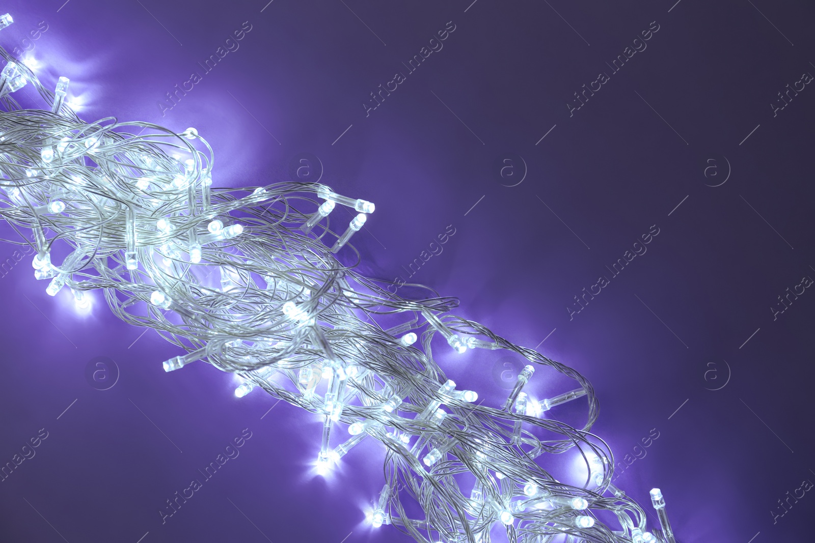 Photo of Glowing Christmas lights on dark violet background, top view. Space for text