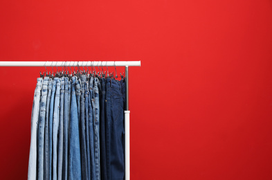 Rack with stylish jeans on red background. Space for text