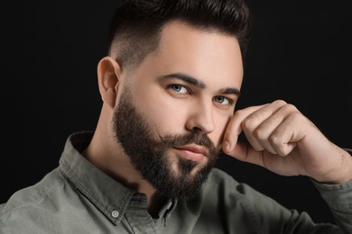 Photo of Young man in shirt touching mustache on black background