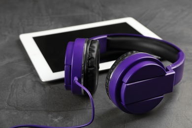 Photo of Stylish headphones and modern tablet on dark table