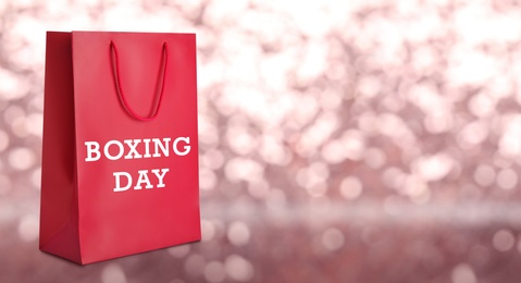 Image of Red shopping bag with text Boxing Day on blurred pink background, closeup. Space for text