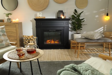 Photo of Stylish fireplace near comfortable armchairs and coffee table with tea in cosy living room. Interior design