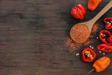 Different ripe chili peppers and spoon with spice on wooden table, flat lay. Space for text