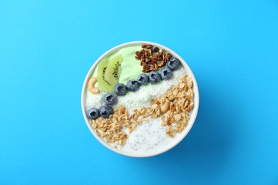 Photo of Tasty smoothie bowl with fresh kiwi fruit, blueberries and oatmeal on light blue background, top view