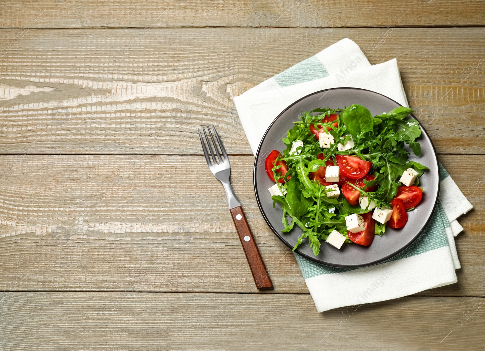 Photo of Delicious salad with feta cheese, arugula and tomatoes on wooden table, flat lay. Space for text