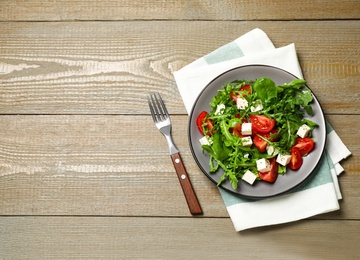 Photo of Delicious salad with feta cheese, arugula and tomatoes on wooden table, flat lay. Space for text