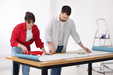 Photo of Woman and man applying glue onto wallpaper sheet at wooden table indoors