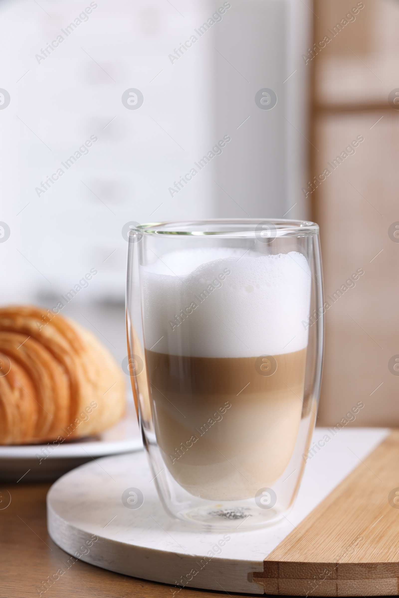 Photo of Aromatic latte macchiato in glass and croissant on wooden table against blurred background