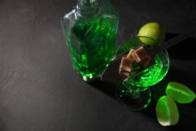 Photo of Absinthe, spoon, brown sugar and lime on black table, top view with space for text. Alcoholic drink