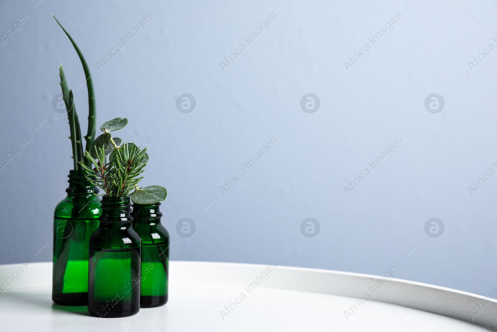 Photo of Glass bottles of different essential oils with plants on table. Space for text