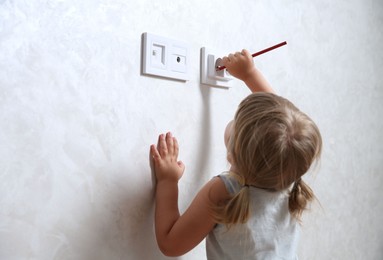 Photo of Little child playing with electrical socket and pencil indoors, space for text. Dangerous situation