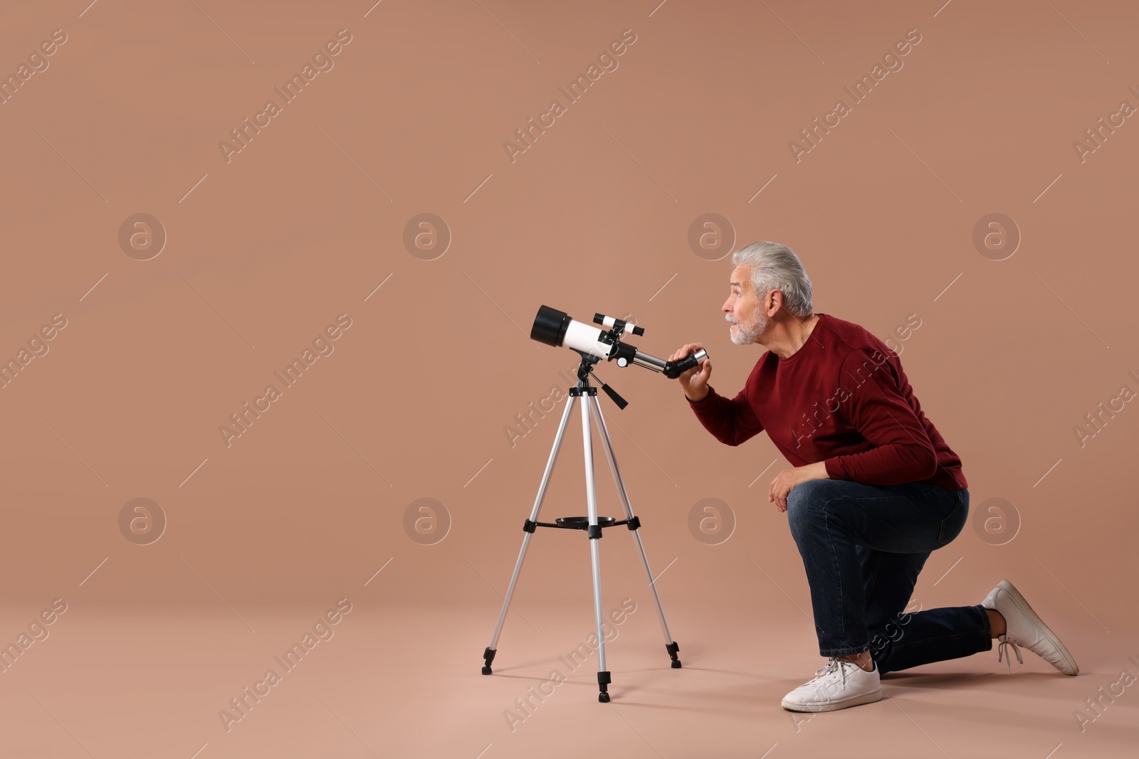 Photo of Senior astronomer with telescope on brown background. Space for text