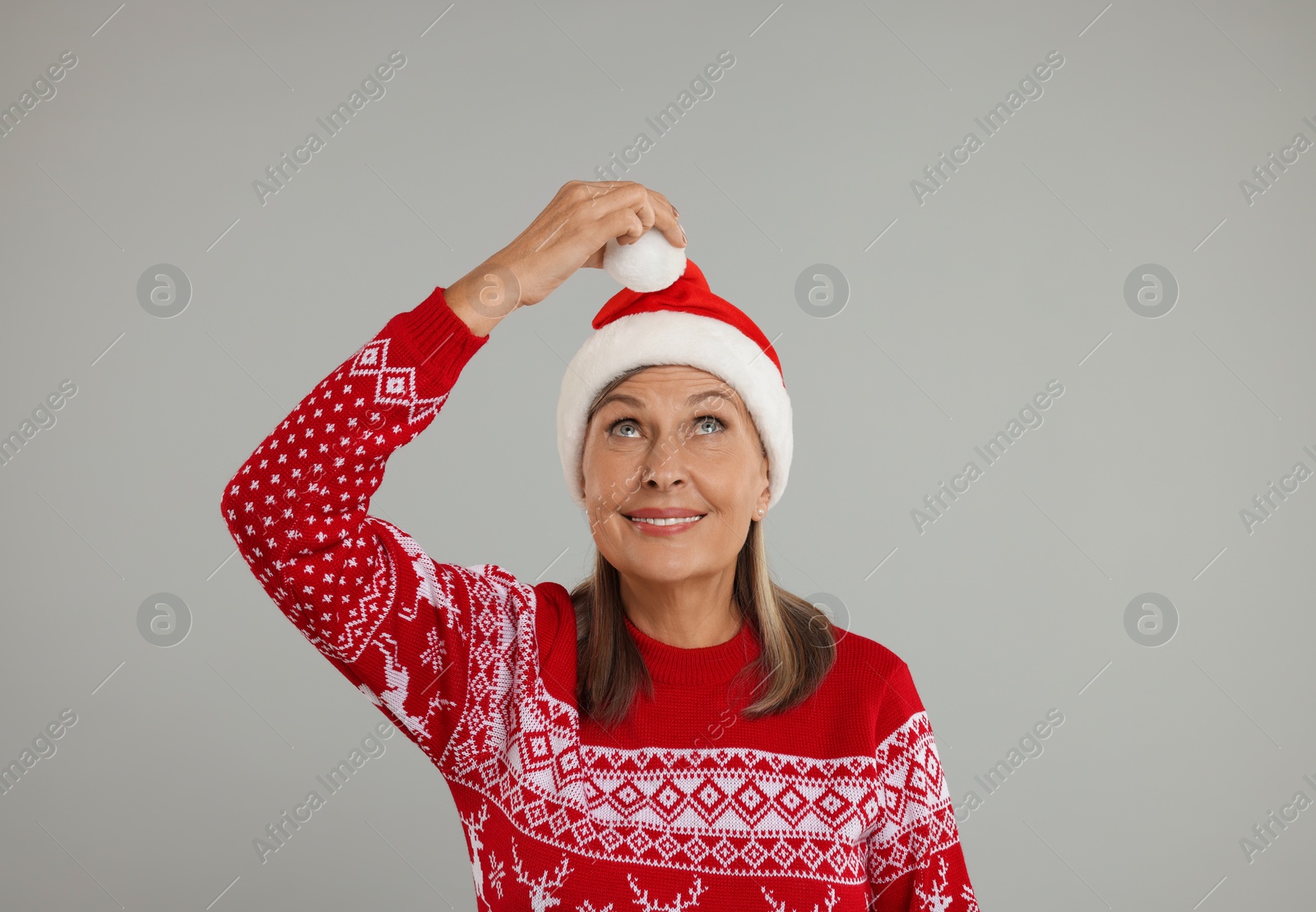 Photo of Happy senior woman in Christmas sweater and Santa hat on grey background